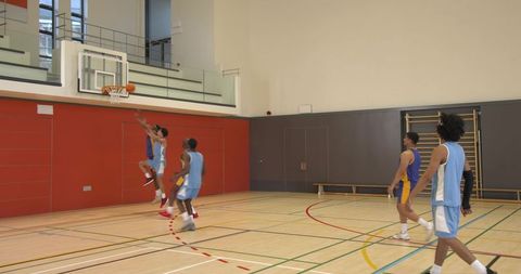 Diverse basketball team jumping for hoop in gymnasium