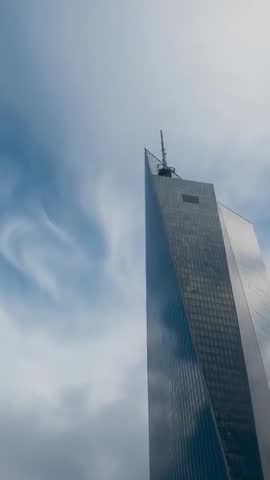 Vertical video of glass skyscraper piercing cloudy sky with reflective spire and antenna