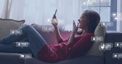 Woman reclining on sofa using smartphone smiling with floating social media engagement icons