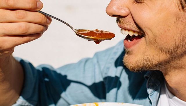Young man enjoying spoonful of tomato sauce closeup smiling casual mealtime moment urban