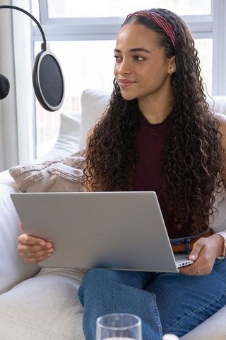African american woman podcasting in cozy home studio with laptop and pop-filter mic