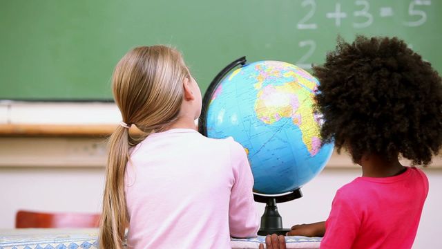 Two children are attentively exploring a globe in a classroom. This image highlights concepts of global awareness, unity, and education, making it ideal for educational materials, school websites, or diversity promotion.