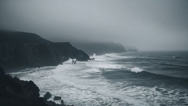 Misty rugged coastline crashing waves against cliffs stretching into foggy horizon