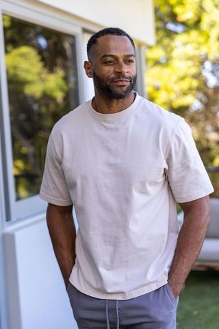 Mature african american man standing on sunlit patio wearing beige tee relaxed portrait