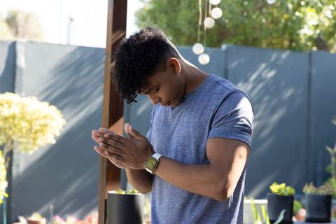 African american man rubbing hands while checking smartwatch on sunlit backyard patio