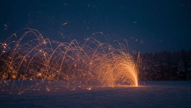 Spinning steel wool sending golden sparks arcing across snow-covered field at night