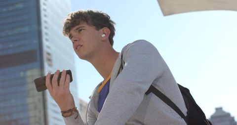 Teen wearing white earbuds and using smartphone while commuting through downtown skyline