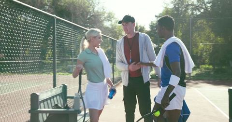 Tennis coach guiding two players on sunlit outdoor court bench during practice
