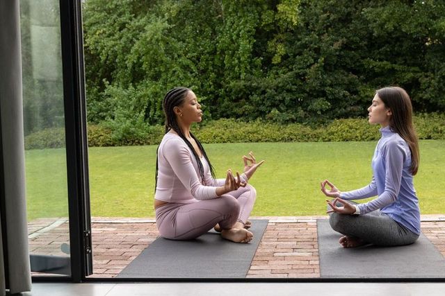 Diverse women practicing outdoor meditation on patio in pastel activewear, mudra pose