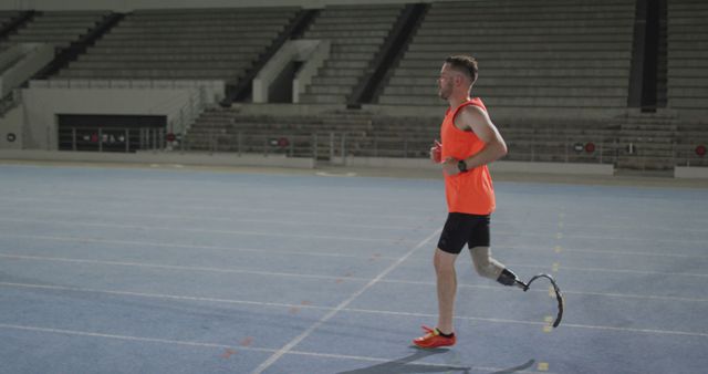 A male athlete with a prosthetic leg is running on an indoor track. He is wearing an orange tank top and running shoes, expressing determination and strength through his workout. Ideal for use in articles or campaigns related to disability sports, inclusivity, motivation, health and fitness, and perseverance.