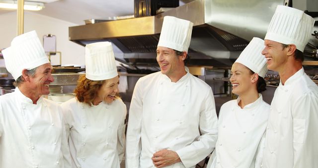 Chefs in white uniforms and tall hats laughing together in professional kitchen. Suitable for illustrating teamwork, culinary arts, gastronomy, and positive workplace environments. Ideal for restaurant industry marketing, cookbooks, culinary school materials, and articles on professional kitchens.