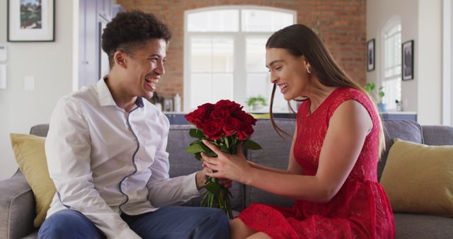 Couple is sitting on sofa smiling while holding red roses, perfect for themes relating to love, romance, and special celebrations. Ideal for advertising relationships, romantic gifts, Valentine's Day promotions, and lifestyle blogs.