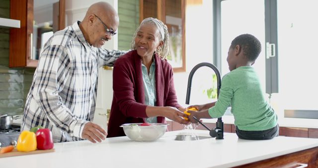 Grandparents and a young boy are engaging in washing dishes together in a modern kitchen. The synergy between different generations completing household chores helps promote family bonding and demonstrates teamwork. This can be used for content related to family life, household chore participation, grandparent and grandchild activities, or healthy family dining habits.