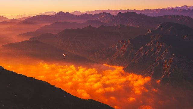 This image captures a breathtaking sunrise casting a golden glow over a misty mountain range. The warm light illuminates the fog settled between peaks, creating a stunning and serene landscape. Perfect for use in travel brochures, nature magazines, or motivational posters highlighting adventure and natural beauty.