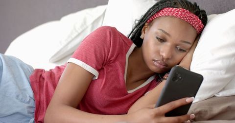 Young Woman Relaxing in Bed Browsing Smartphone Content