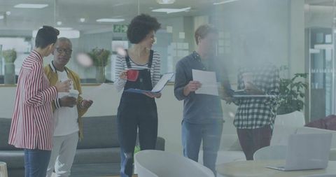 Young Diverse Team Collaborating in Modern Office Lounge Holding Coffee and Papers