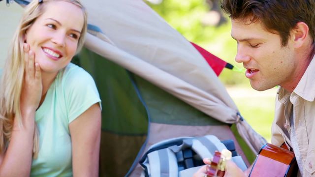 Couple enjoying a serene moment outdoors with a romantic guitar performance at a camping site. Great for promoting outdoor music, camping gear, romantic getaways, and leisure activities in nature.