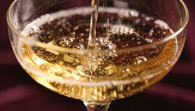 Pouring golden sparkling champagne into coupe glass creating concentric bubbles