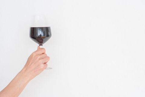 Hand holding red wine glass over white minimalist background