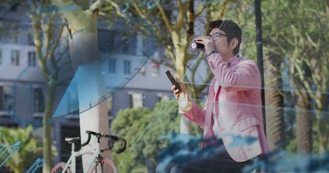 Asian man sipping coffee and checking smartphone beside bicycle with blue data overlays