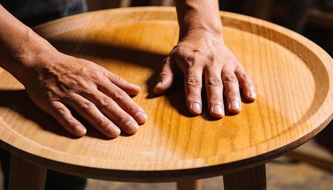 Pressing hands on sanded round wooden stool top showing wood grain and craftsmanship
