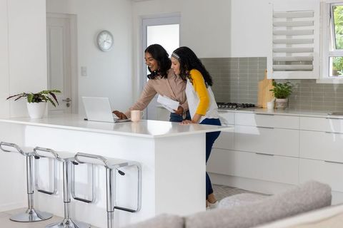 Mother and teenage daughter collaborating on budget using laptop at bright kitchen island