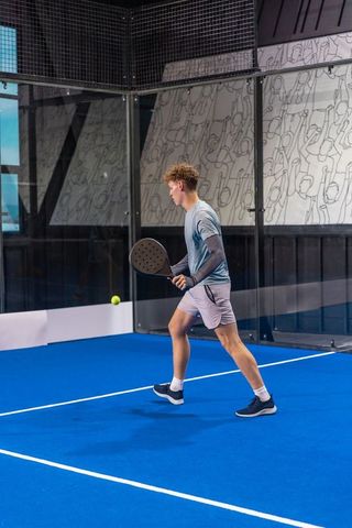 Young athlete lunging for yellow ball on modern blue padel court, dynamic sports action