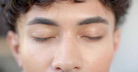 Young male resting with eyes closed closeup showing smooth skin texture and curly hair