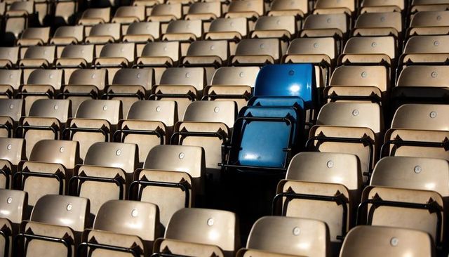 Bright blue seats standing out among repeating beige stadium chairs in sunlit bleachers