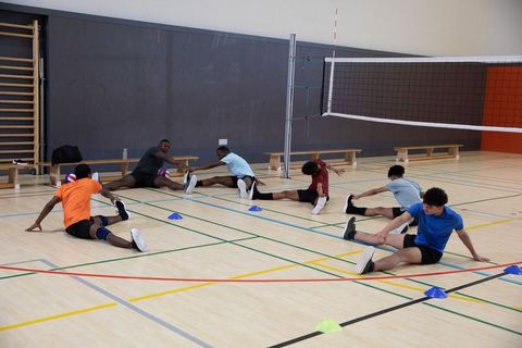 Men stretching together on indoor volleyball court during dynamic warmup mobility drill