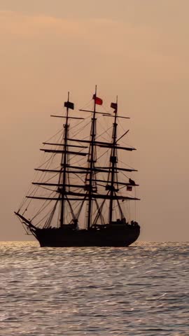 Three-masted tall ship gliding at dusk over calm sea, flags fluttering | Vertical video