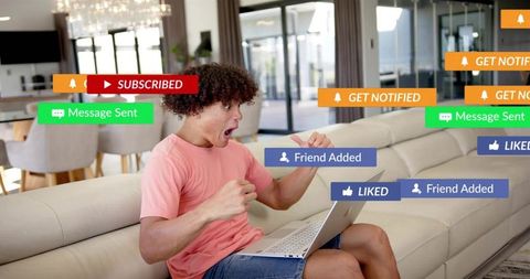 Young man reacting to flood of social media notifications on laptop while sitting on sofa