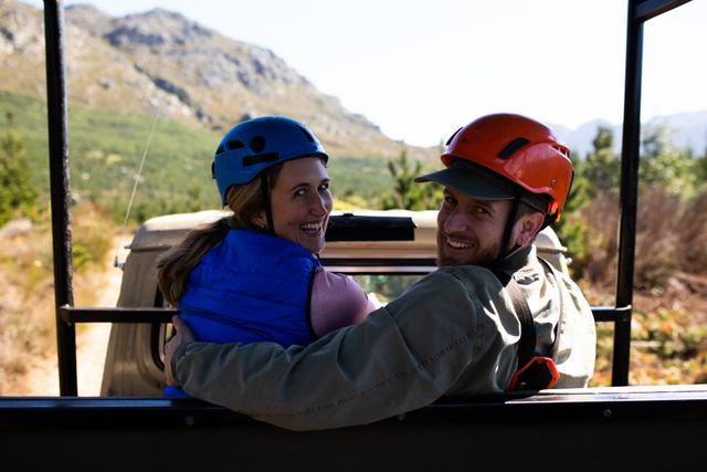 Portrait of a Caucasian couple enjoying time in nature together, wearing zip lining equipment sitting in a car, looking back on a sunny day in mountains. Fun adventure vacation weekend.