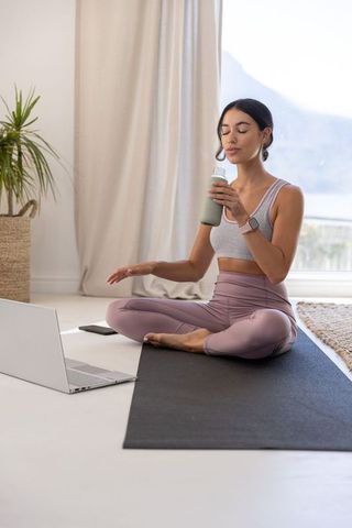 Sipping green smoothie during home yoga session with laptop for mindful wellness
