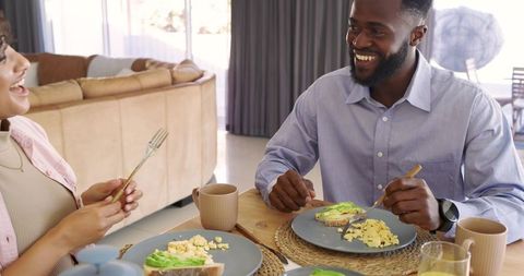 Smiling couple sharing relaxed morning breakfast at home with avocado toast and scrambled eggs