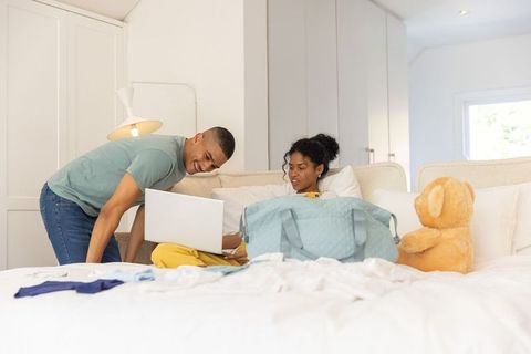African american couple sharing laptop on bed while packing duffel, relaxing in bedroom