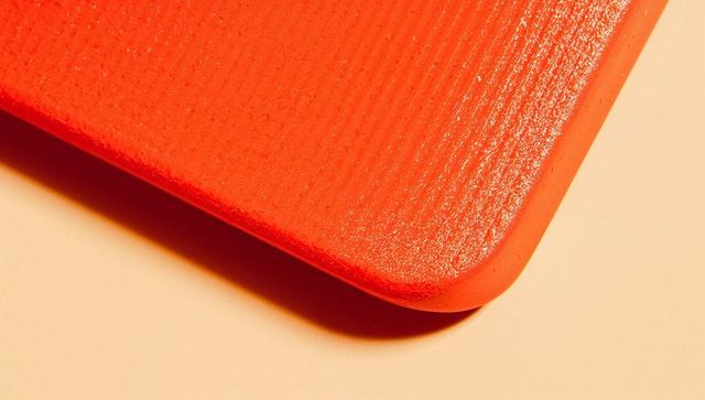 Glossy red textured panel with rounded corner on warm beige background, macro minimalist design