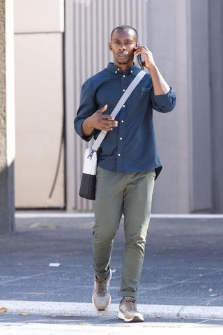 African man walking and talking on smartphone wearing navy shirt and chinos with shoulder bag