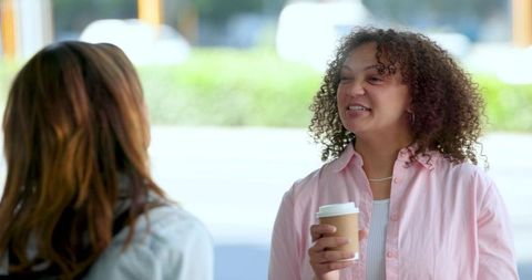 Mixed-race friends chatting over takeaway coffee outside cafe, casual urban conversation