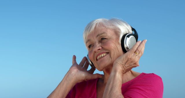A senior Caucasian woman enjoys listening to music on her headphones, with copy space. Her joyful expression suggests the positive impact of music on mood and well-being in older adults.