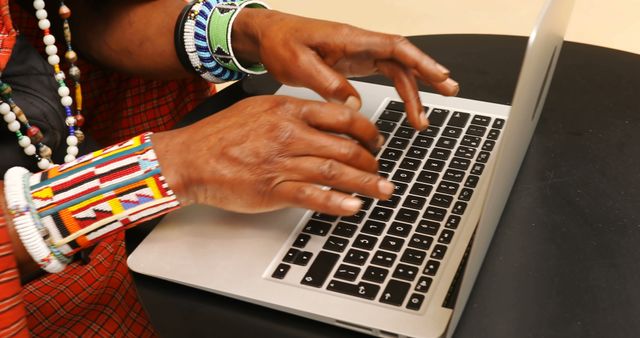 African American man typing on a laptop at home. Traditional bracelets add a cultural touch as he works on his computer.