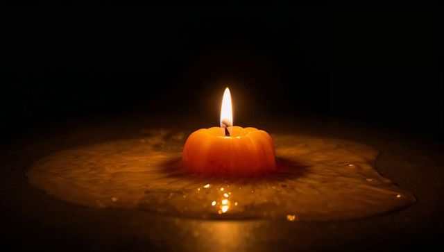 Flickering orange candle on reflective surface with melted wax pool