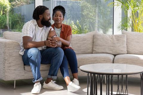 Couple sitting closely on sunlit modern sofa holding hands and sharing intimate, relaxed moment