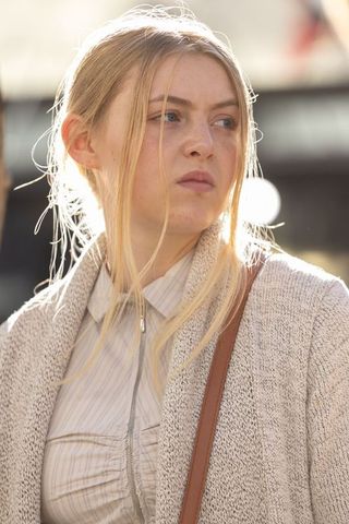 Young woman standing in sunlit urban street wearing knit cardigan and leather bag strap