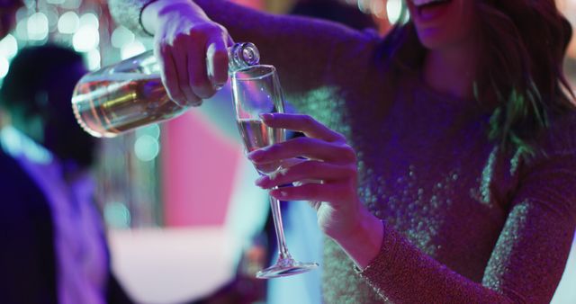 Image of midsection of smiling caucasian woman pouring sparkling wine into glass at a nightclub. Fun, drinking, going out and party concept.