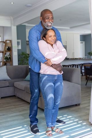 Diverse mature couple embracing in sunlit home living room showing warmth and affection