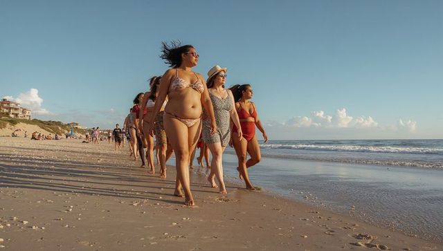 Confident women walking along sunlit beach at golden hour wearing diverse swimwear