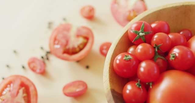 Photo displays vibrant cherry tomatoes in a rustic wooden bowl. Sliced tomatoes and seeds scattered around add texture and depth. Perfect for blogs, culinary websites, cooking magazines, and advertisements promoting healthy eating and fresh produce.