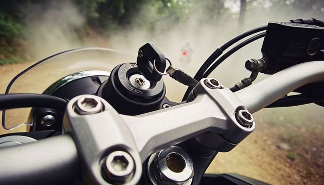 Motorbike handlebars closeup with key in ignition on dusty forest trail, adventure riding