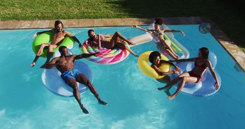 Group of friends floating on colorful pool floats laughing and relaxing in backyard summer